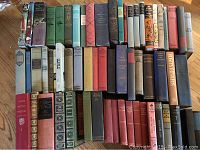 Photo showing an array of antique and vintage hardcover books arranged standing upright and laid down on a wooden surface, titles include classics like War and Peace