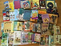 Photo showing a large assortment of over 40 children's books, both new and vintage, scattered and stacked. Various cover arts from classic fairy tales, interactive jigsaw books, to storybooks are visible.