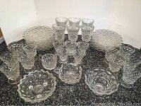 Photo showing large stack of 13 dessert plates at the back, multiple large, medium, small glasses in front, and several small dishes in front center.