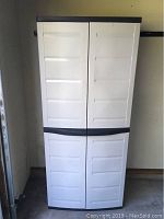 Front view of closed white plastic storage cabinet with black trim.