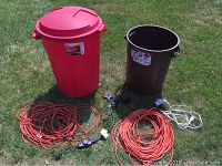 All items together on lawn: red Rubbermaid can, brown Ruffneck can, orange extension cords, two timers