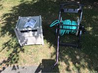 Two hose reels side by side outdoors on grass, one open frame metal/plastic reel with blue hose, one closed plastic storage box reel.
