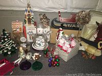 Overview photo showing Thomas Kinkade snowman figurine, ceramic Christmas tree, sleigh, wrapped gifts, and other assorted holiday decorations on a carpeted floor with neutral backdrop.