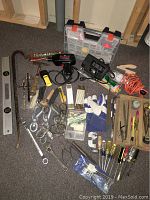 Wide view of the assortment of household tools including clamps, screwdrivers, drill, jigsaw, level, hammer, gloves, bits, and accessories arranged on floor.
