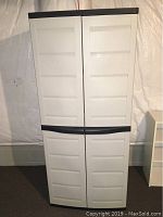 Front view of closed plastic storage cabinet, white with black edges and handles.