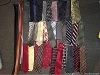 Top view of various men's neckties laid out horizontally and vertically on a carpet. Several colors and patterns present.