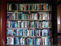 Six-shelf bookcase filled with assorted hardcover and paperback books