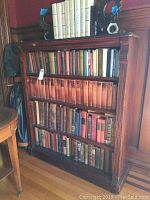 Wooden bookshelf filled with about 100 hardcover books with varied colors and sizes, mainly vintage style.
