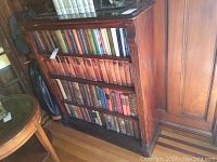 Full view of the antique wooden bookcase with four shelves filled with books.