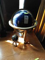 Large blue globe on brass stand and smaller decorative stone orb on brass base shown together on wooden surface under natural light.
