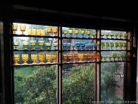 Full view of amber, green, and blue goblets displayed on window shelf, showcasing various sizes and embossed designs.