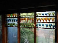 Front view of multiple shelves filled with colorful glassware in amber, blue, and green colors displayed in rows