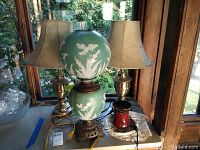 Full view of all items: a pale green glass lamp with floral motif, two metal urn motif lamps with cream shades, and a brown ceramic candle warmer.