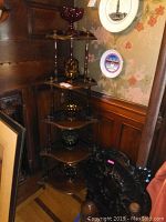 Full view of the wood corner shelf placed in a corner, showing five tiers and dark wood finish.
