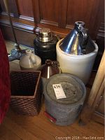 Overall view of jugs, thermos, minnow bucket and wicker basket on a wooden floor with furniture around