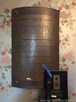 Front view of large curved metal nameplate with embossed text for The New Britain National Bank, showing mounting hardware and patina.