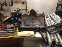 Overview of tools on table including Milwaukee drill, metal pipes, saws, and various hand tools.