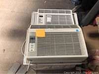 Photo of two white window air conditioner units stacked, LG in back, Sharp in front.