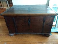 Front view of wooden trunk showing metal decorative strips and ring pulls, and bun feet.