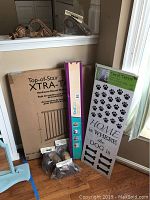 Photo showing boxed Top-of-Stair XTRA-TALL wood gate, K12 stairway gate installation kit box, wall decal package with dog paw prints and bones, and hardware components in bags.