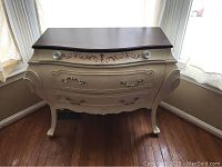 Front view of vintage dresser showing off-white body, two large drawers with ornate handles, top drawer with red stencil design and glass pull knobs, and dark wood stained top surface.
