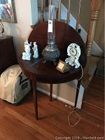 Photo showing the wooden demi-lune half-moon table in folded state with several decorative items on top including a metal oil lamp, two figurines, and a clock.
