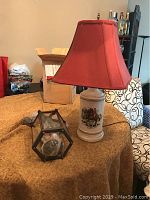 Vintage equestrian table lamp with red fabric shade and unused hanging light fixture on a table.