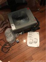 3M 9100 Series overhead projector on floor with accessories including power cord and manual, showing unit condition.