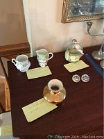Wide view of the lot items displayed on dark wood table including Bavaria Orleans series cream and sugar set, bisque cherub item, cut glass candlestick holders, and gold painted Holley Ross vase.