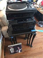 Photo showing a stack of stereo components on a small black side table with carved legs and a vinyl record album propped in front featuring Music Man cover art.