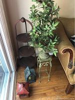Photo showing the three-tier wooden plant stand, iron plant stand, faux plant, and two candle lanterns on the floor