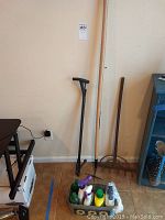 Photo of gardening tools including wooden rake, diamond hoe, weed grabber, and plastic bottles of chemicals and feed with metal bucket.