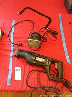 Craftsman electric reciprocating saw and black metal hand saw frame on red fabric