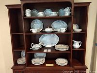 Shelved set of blue patterned porcelain dinnerware pieces including plates, cups, platters, pitcher, and gravy boat.