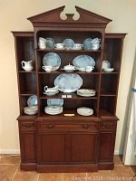 Front view of wooden breakfront displaying dimensions, build, and contents on shelves (blue and white dishware) which are excluded from sale.