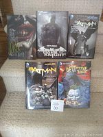 Five Batman hardcover comic books arranged in two rows, showing covers featuring Batman and the Joker.