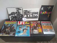 Photo showing two black and white Beatles pictures and four Beatles-related vintage magazines arranged on a bench.