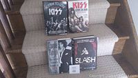 Five rock biography books arranged on carpeted stairs, front covers displayed, featuring KISS, Purple Reign, and Slash
