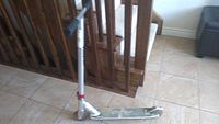 Side view of silver Razor kick scooter with black foam handlebars and foldable mechanism, placed indoors on tiled floor.