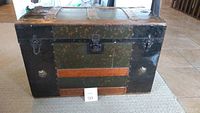 Front view of the antique trunk showing metal body with wooden reinforcements, metal lock clasp on front.