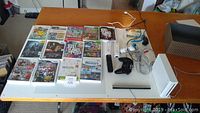 Entire Wii console setup with games, controllers, sensor bar, and cables on white table.