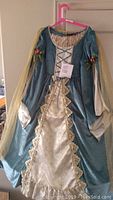 Full view of the blue and cream princess dress with lace-up front, bell sleeves with gold netting, rose embellishments, and gold lace trim on skirt.