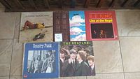 Photo of five vintage vinyl records arranged on a tile floor, showing front covers from a variety of artists.