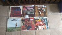 Photo shows six vinyl record album covers arranged in two rows of three on tiled floor