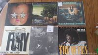 Photo showing six used vinyl records arranged in two rows of three, various album covers visible including woman with star sunglasses, natural landscape, and Koko Taylor singing.