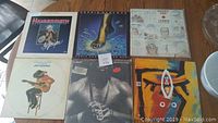 Photo of six vinyl records with various artists and album covers, placed on a wood surface.