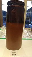 Tall vintage West Germany floor vase in brown gradient glaze shown standing on a white surface near a window with other glassware in the background.