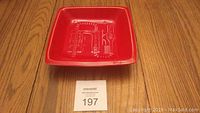 Red square ceramic dish with abstract embossed design on interior and promotional markings on underside.