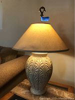 Front view of one resin base table lamp with fabric-covered paper shade illuminated revealing lampshade texture and design.