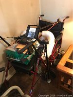 Photo showing red travel wheelchair with black seat, control panel device placed on seat, and assorted accessories on and around chair